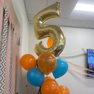 A balloon of the number five surrounded by blue and orange balloons