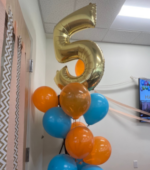 A balloon of the number five surrounded by blue and orange balloons