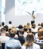 A group of people listen to a speaker making a presentation