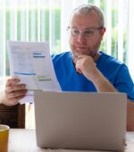 A nurse looks over bills in front of their computer