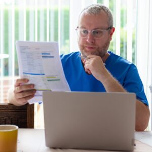 A nurse looks over bills in front of their computer