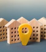 wooden blocks shaped like houses with a yellow destination pin in front-center
